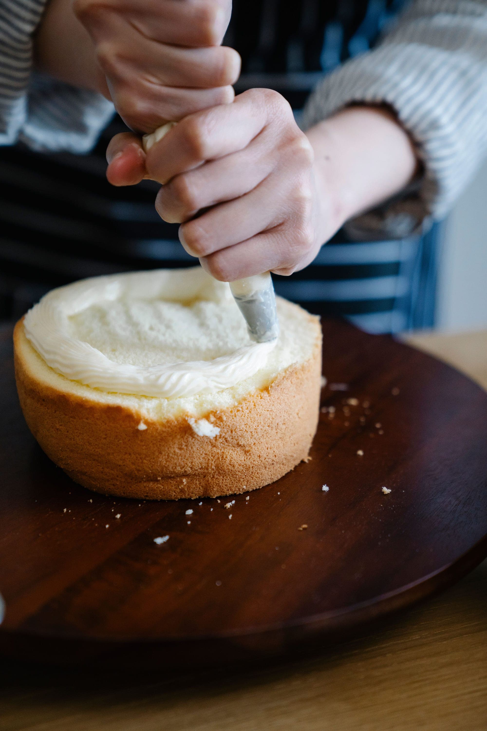 Bolo recebendo recheio de creme sobre base de madeira